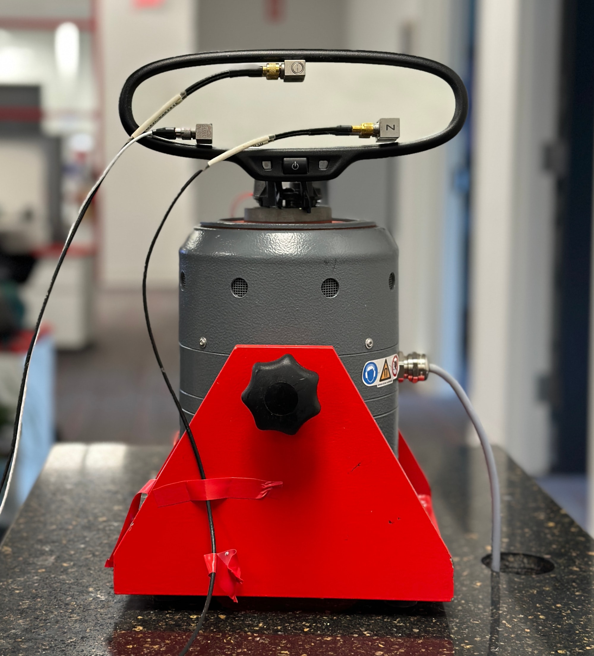 A tabletop shaker setup with an internal rearview mirror mounted to the shaker head and three accelerometers mounted to the mirror lens in a triangle formation.